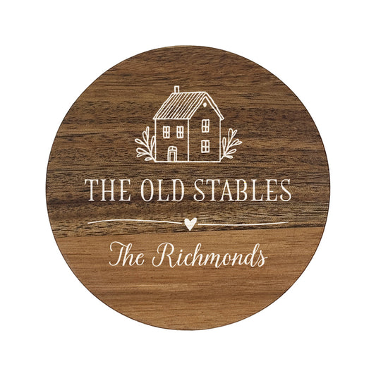 Wooden round coaster with house illustration and personalised house name and family name in white text.