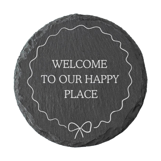 Round slate coaster with 'Welcome to our happy place' text on a white background