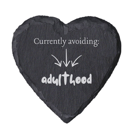 Heart-shaped slate coaster with text 'Currently avoiding: adulthood' on a white background