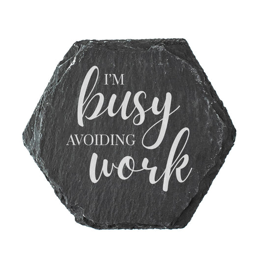 Hexagonal black slate coaster with 'I'm busy avoiding work' text on a white background