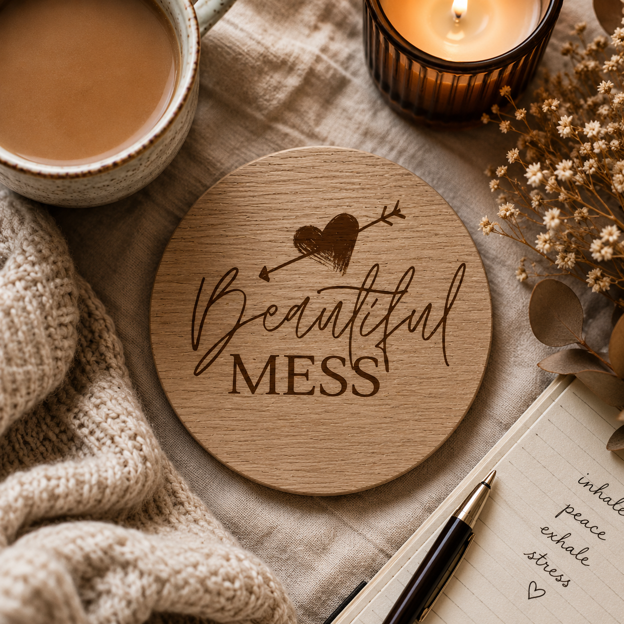 Wooden coaster with 'Beautiful Mess' text on a table with coffee, candle, and notebook.