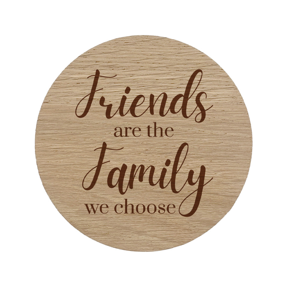 Round wooden coaster with engraved text 'Friends are the family we choose' on a white background