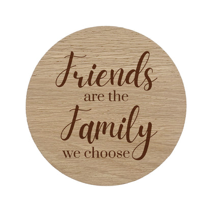 Round wooden coaster with engraved text 'Friends are the family we choose' on a white background