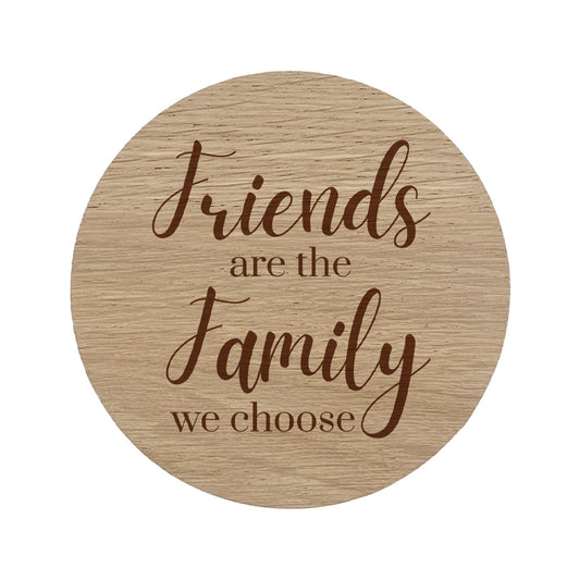 Round wooden coaster with engraved text 'Friends are the family we choose' on a white background
