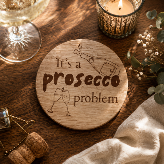 Round wooden coaster with "it's a prosecco problem" text on a wooden surface with prosecco glass and cork.