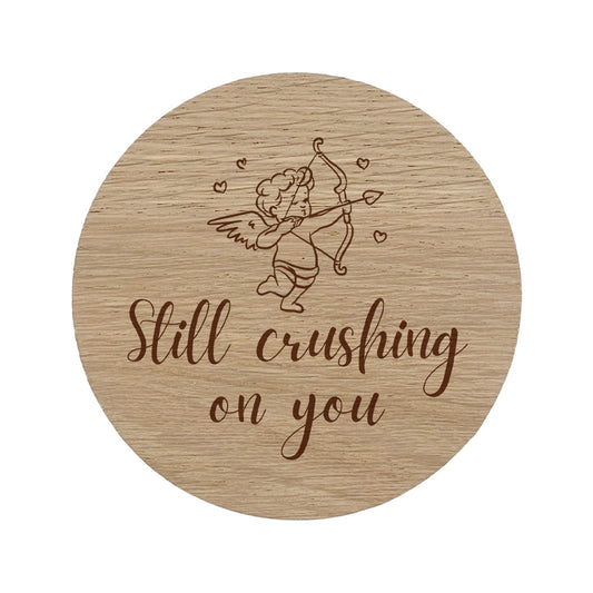 Round wooden coaster with cupid illustration and 'Still crushing on you' text
