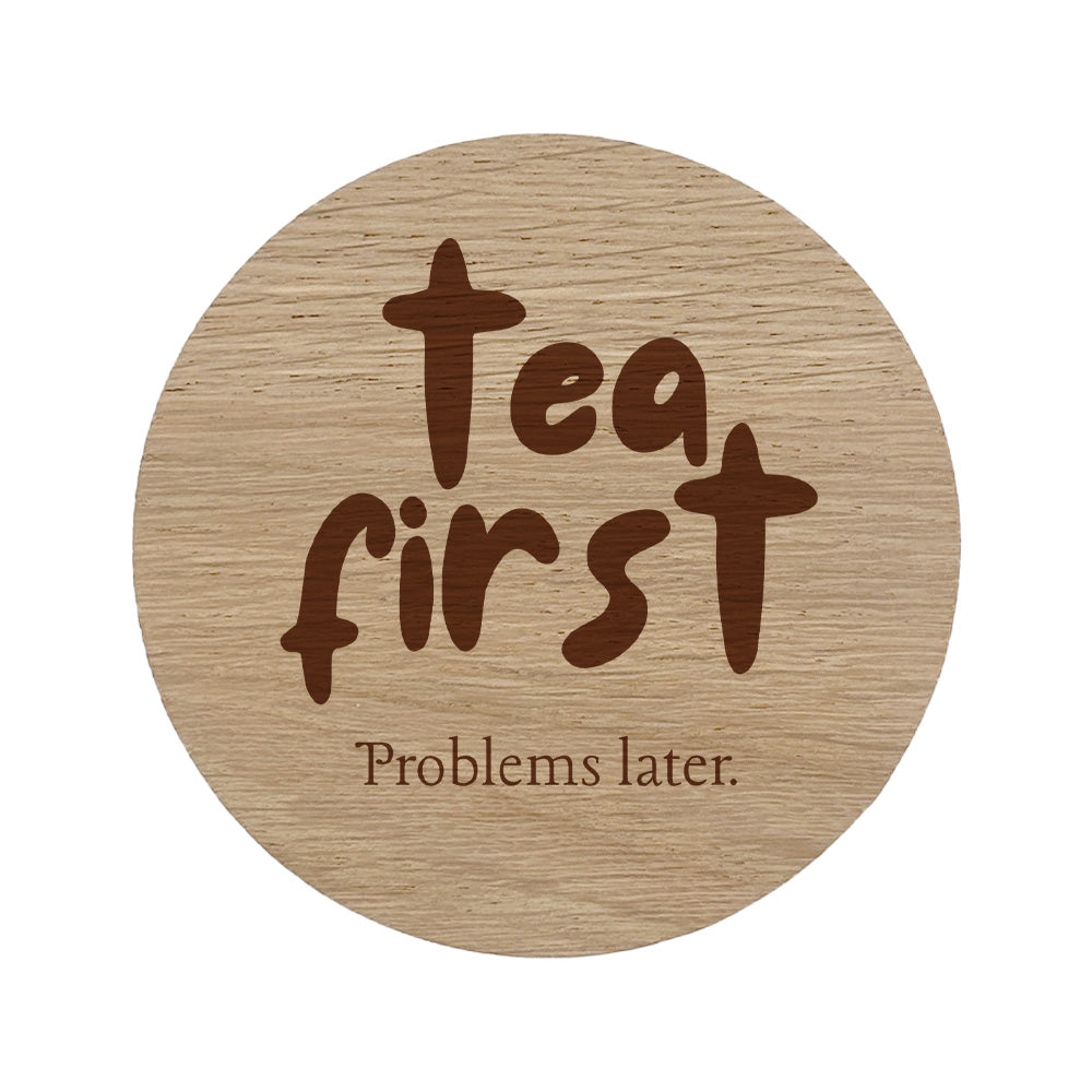 Round wooden coaster with 'Tea first, Problems later' text on a white background