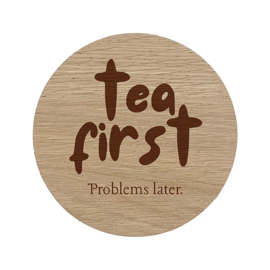 Round wooden coaster with 'Tea first, Problems later' text on a white background