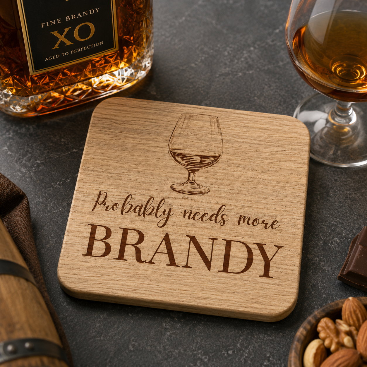 Square wooden coaster with "probably needs more brandy" text and brandy glass illustration, on a bar with brandy bottle and glass.