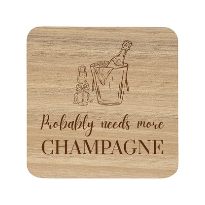 Square wooden coaster featuring the funny quote "Probably needs more champagne" in crisp lettering with a champagne bottle and glass illustration