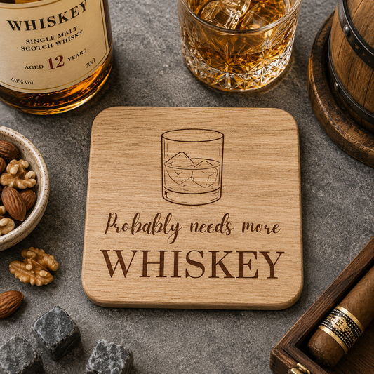 Square wooden coaster with 'Probably needs more whiskey' text and whiskey glass illustration on a bar with whiskey bottle and barrel.