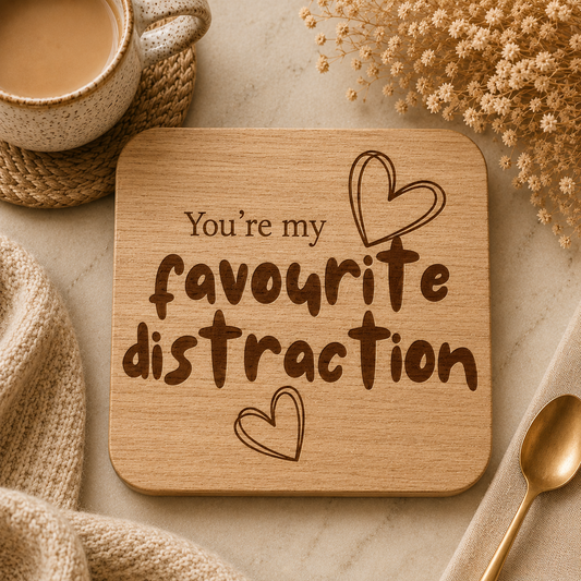 Square wooden coaster with the quote 'You're my favourite distraction' and heart illustrations on a stone work surface with cup of tea.