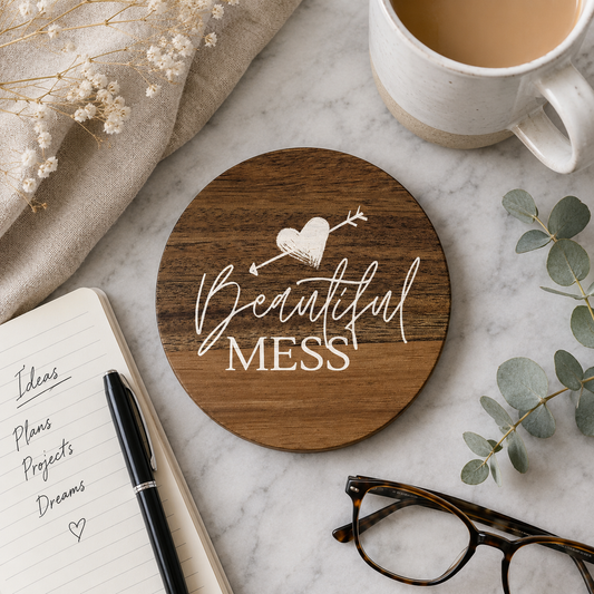 Round wooden coasters with 'Beautiful mess' text in white lettering, on a marble work surface with a cup of tea.