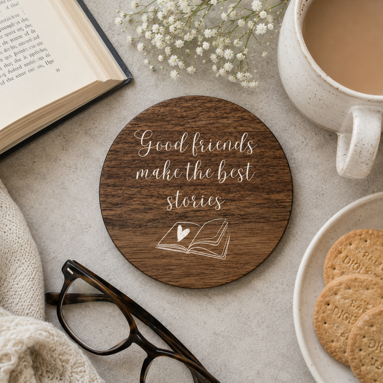 Wooden coaster with 'Good friends make the best stories' text, placed on a table with a book, cup of coffee, and cookies.