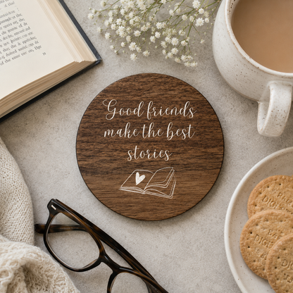 Wooden coaster with 'Good friends make the best stories' text, placed on a table with a book, cup of coffee, and cookies.