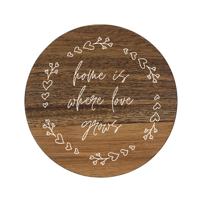 Round wooden coaster with decorative text 'home is where love grows' and heart designs on a white background