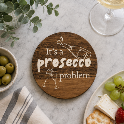 Wooden coaster with 'It's a prosecco problem' text on a table with snacks and a glass of prosecco.