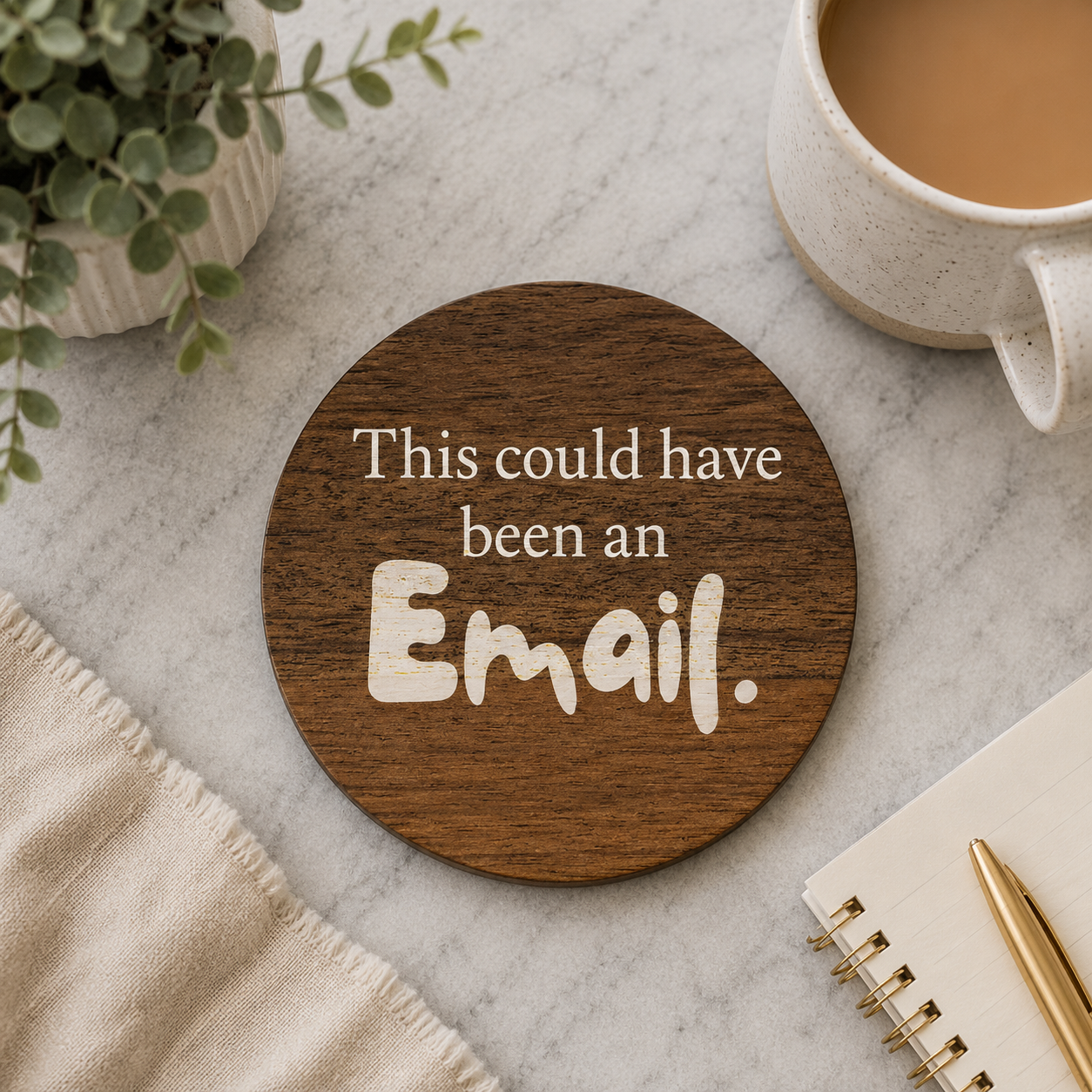 Round wooden coaster with 'This could have been an Email.' text on a marble surface with a cup of coffee and plant.