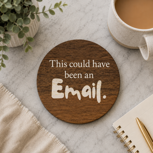 Round wooden coaster with 'This could have been an Email.' text on a marble surface with a cup of coffee and plant.