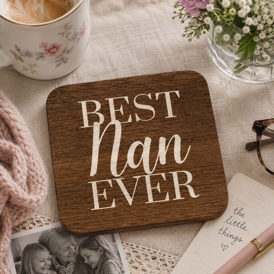Square wooden coaster with 'Best Nan Ever' text on a table with a cup, flowers, and photos.