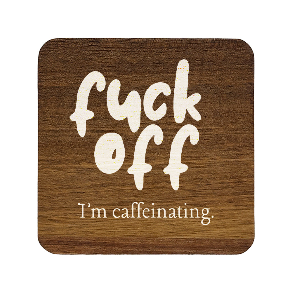 Square wooden coaster with white text 'f*ck off I'm caffeinating.' on a white background