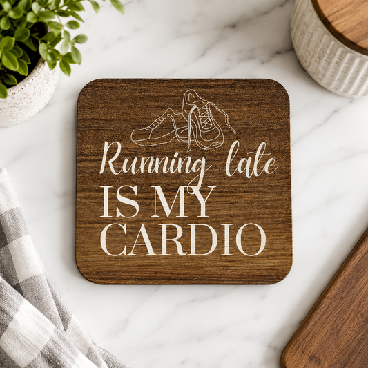 Square wooden coaster with 'running late is my cardio' quote and trainers illustration, on a marble worktop with plants.