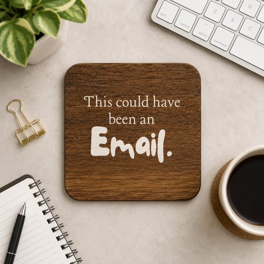 Square wooden coaster with 'this could have been an email' quote on a desk with coffee cup, keyboard and notebook.