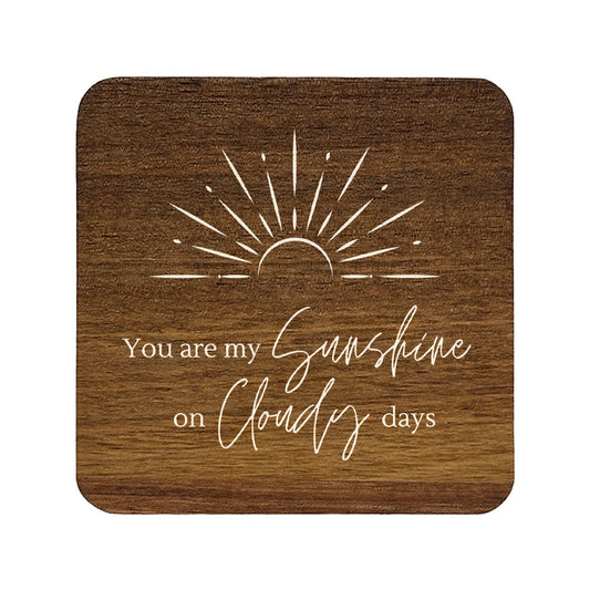 Square wooden coasters with 'you are my sunshine on cloudy days' quote in white text with stylised sunrise illustration.