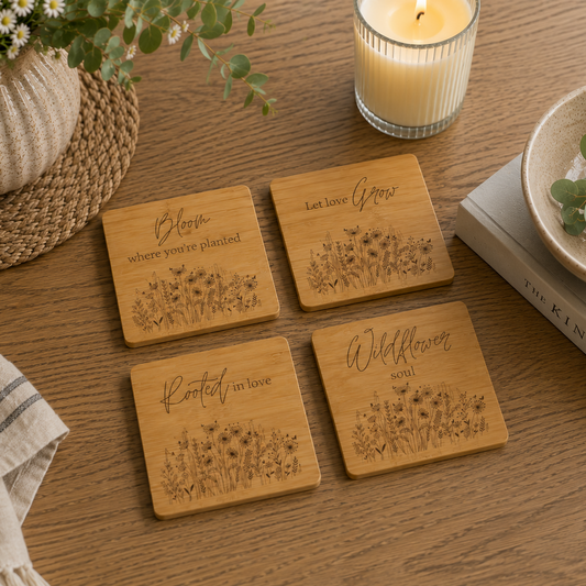 A set of 4 bamboo wood coasters decorated with inspirational quotes and wildflower illustrations. The coasters are set on a wooden coffee table with a candle and plants.