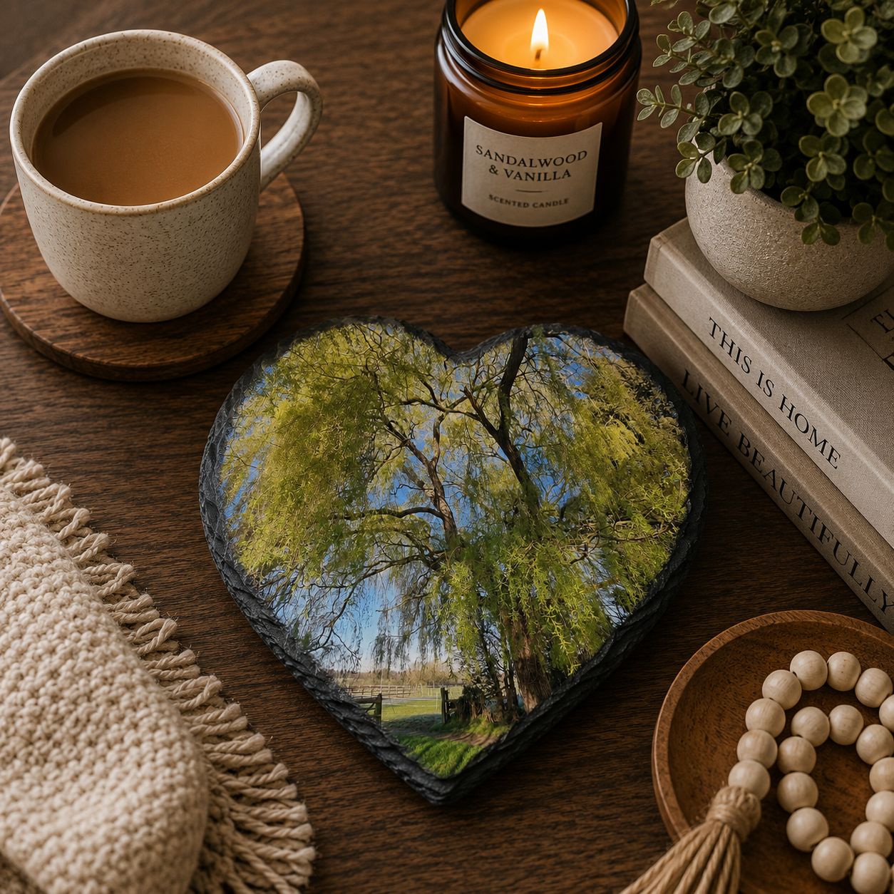 Heart-shaped personalised photo slate coaster with tree photo, cup of coffee, candle, and books on a wooden surface.