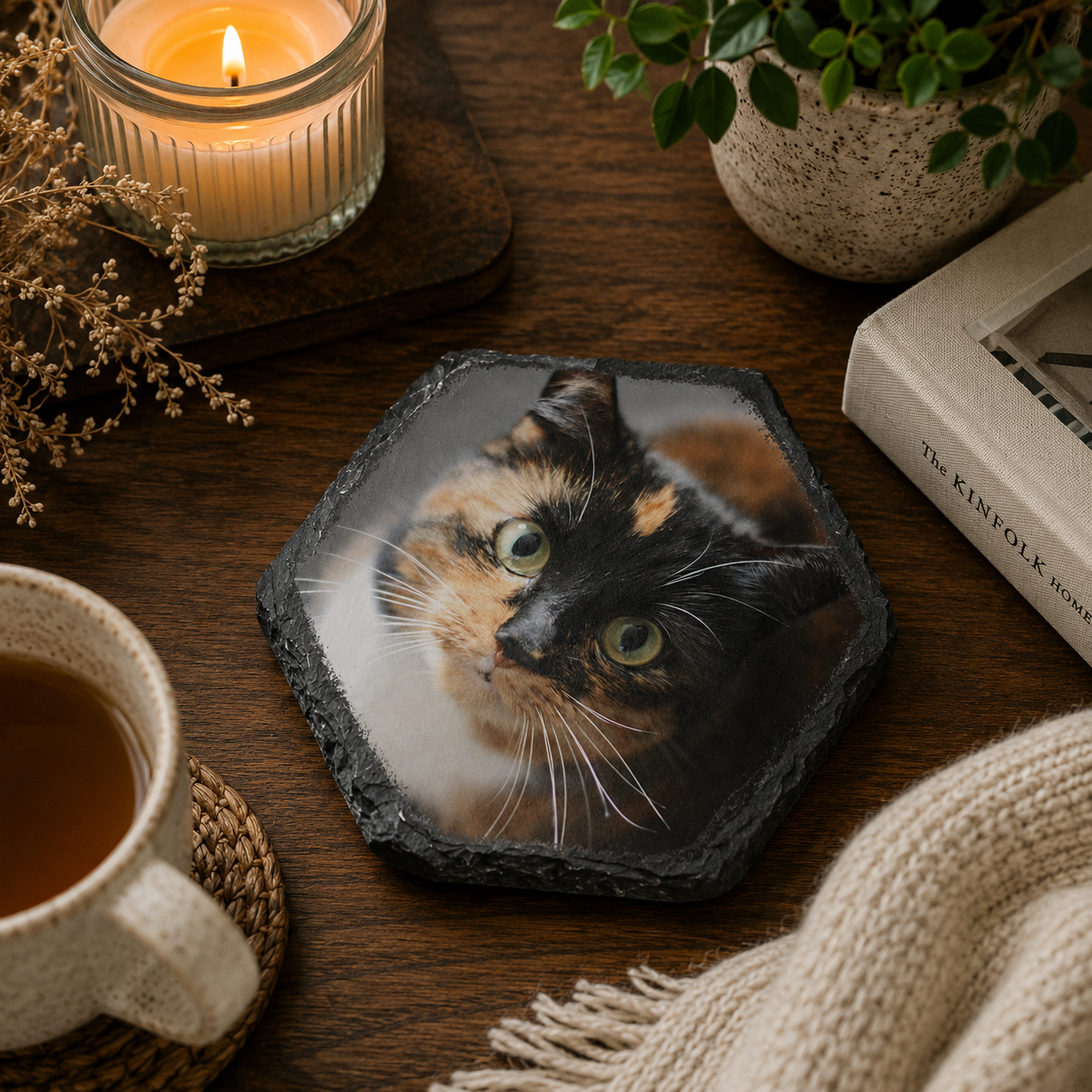Personalised photo hexagonal coaster with a cat's face on a wooden table with a candle, mug, and plant.