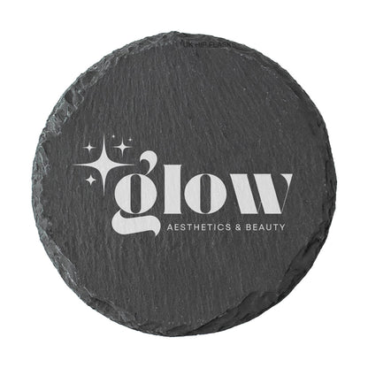A round dark grey slate coaster personalised with a white printed logo for a beauty salon and aesthetics clinic. Your logo here.