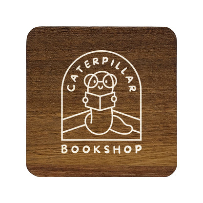 A square wooden coaster with rounded corners, personalised with a book shop business logo in white. Your logo here.