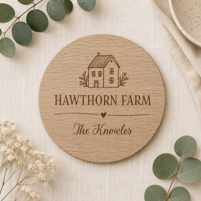 Round wooden coaster with personalised house and family name on a light background with greenery.