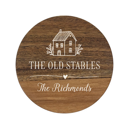 Wooden round coaster with house illustration and personalised house name and family name in white text.