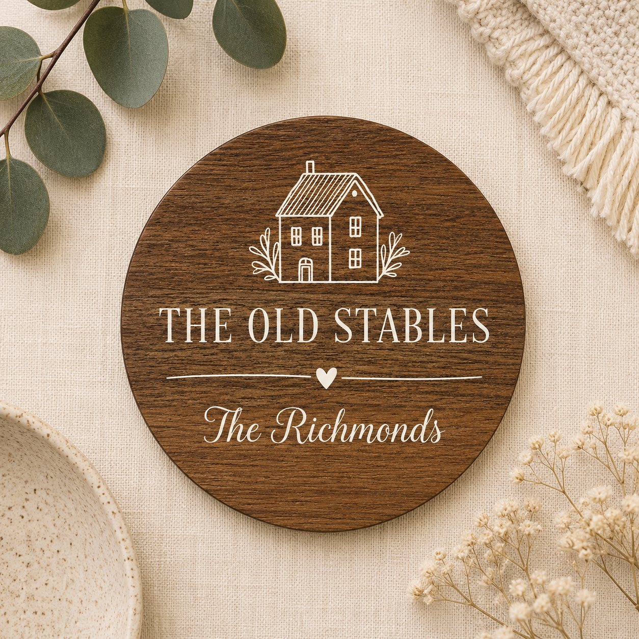 Round wooden coaster with personalised house name and family name text on a beige surface with decorative elements.