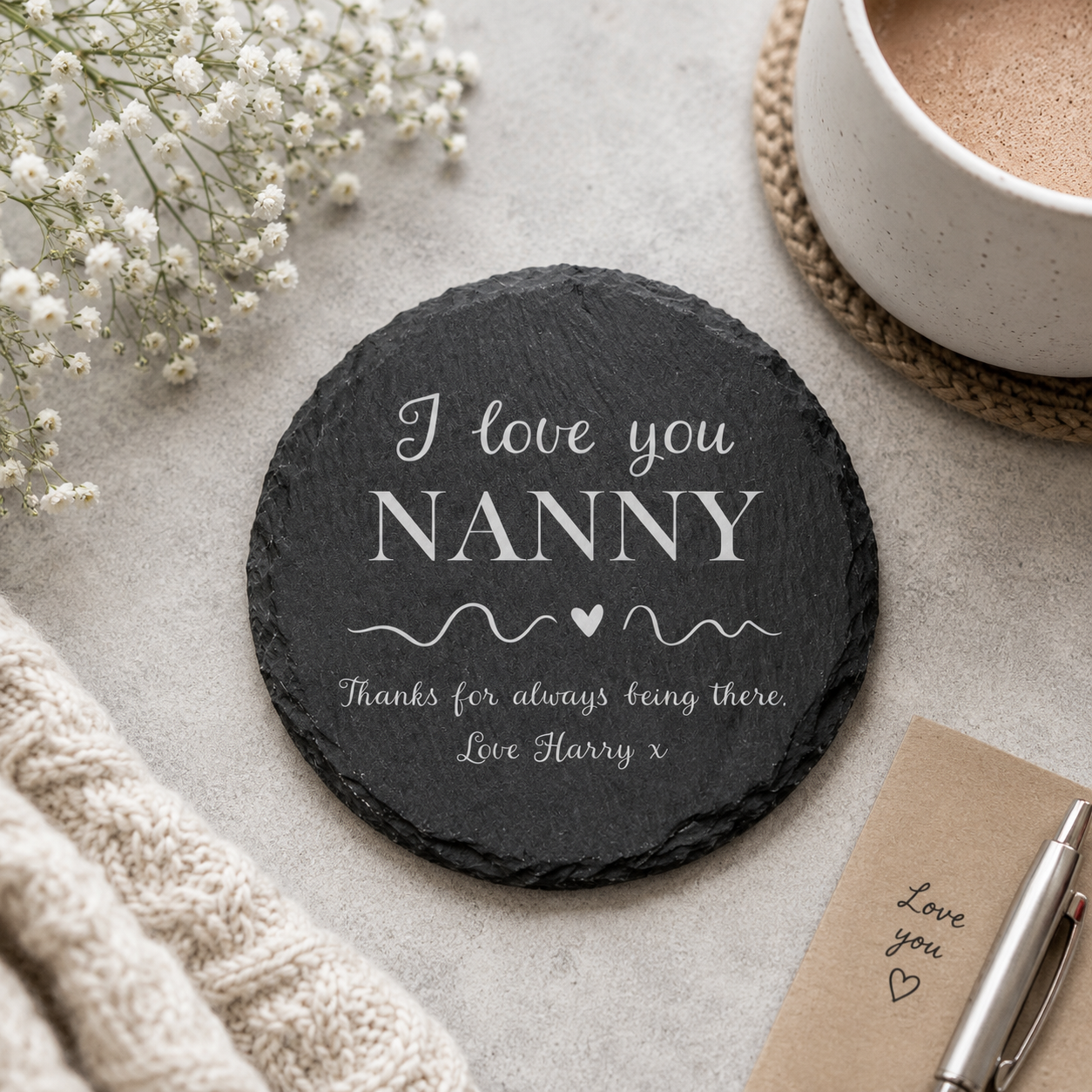Round personalised slate coaster with a name added to the phrase 'I love you, thanks for always being there', on a stone surface with a cup of tea.