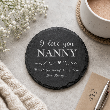 Round personalised slate coaster with a name added to the phrase 'I love you, thanks for always being there', on a stone surface with a cup of tea.