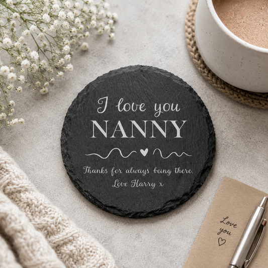 Round personalised slate coaster with a name added to the phrase 'I love you, thanks for always being there', on a stone surface with a cup of tea.