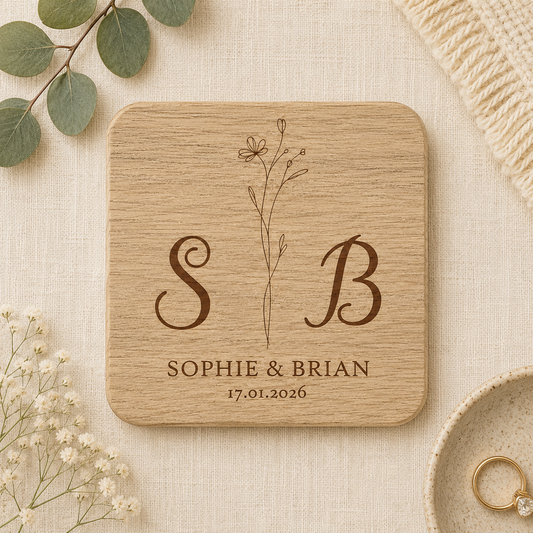 Square wooden coaster with personalised initials, names and date on a beige fabric background with floral elements.