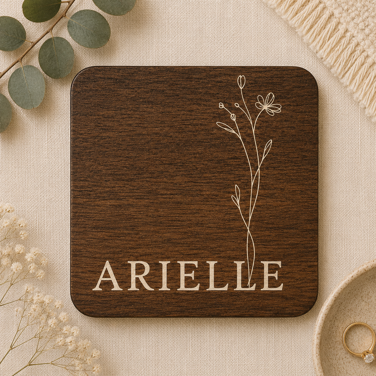Square wooden coaster with personalised name and floral design on a beige surface with decorative elements.