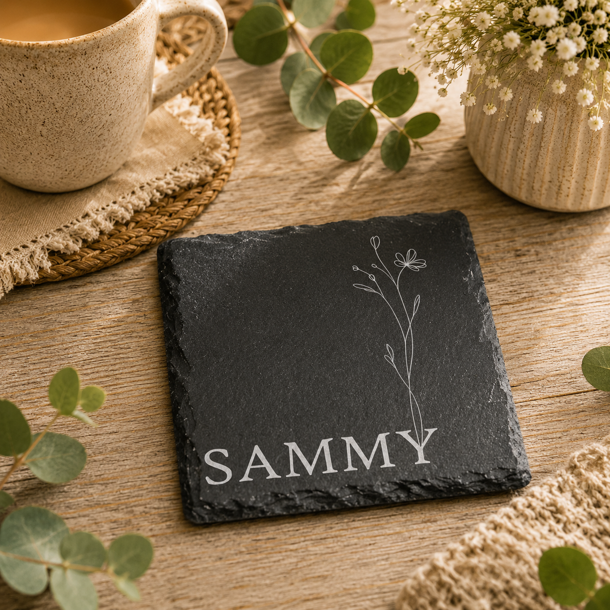 Square slate coaster personalised with a custom name and floral illustration, on a wooden table with a cup of tea.