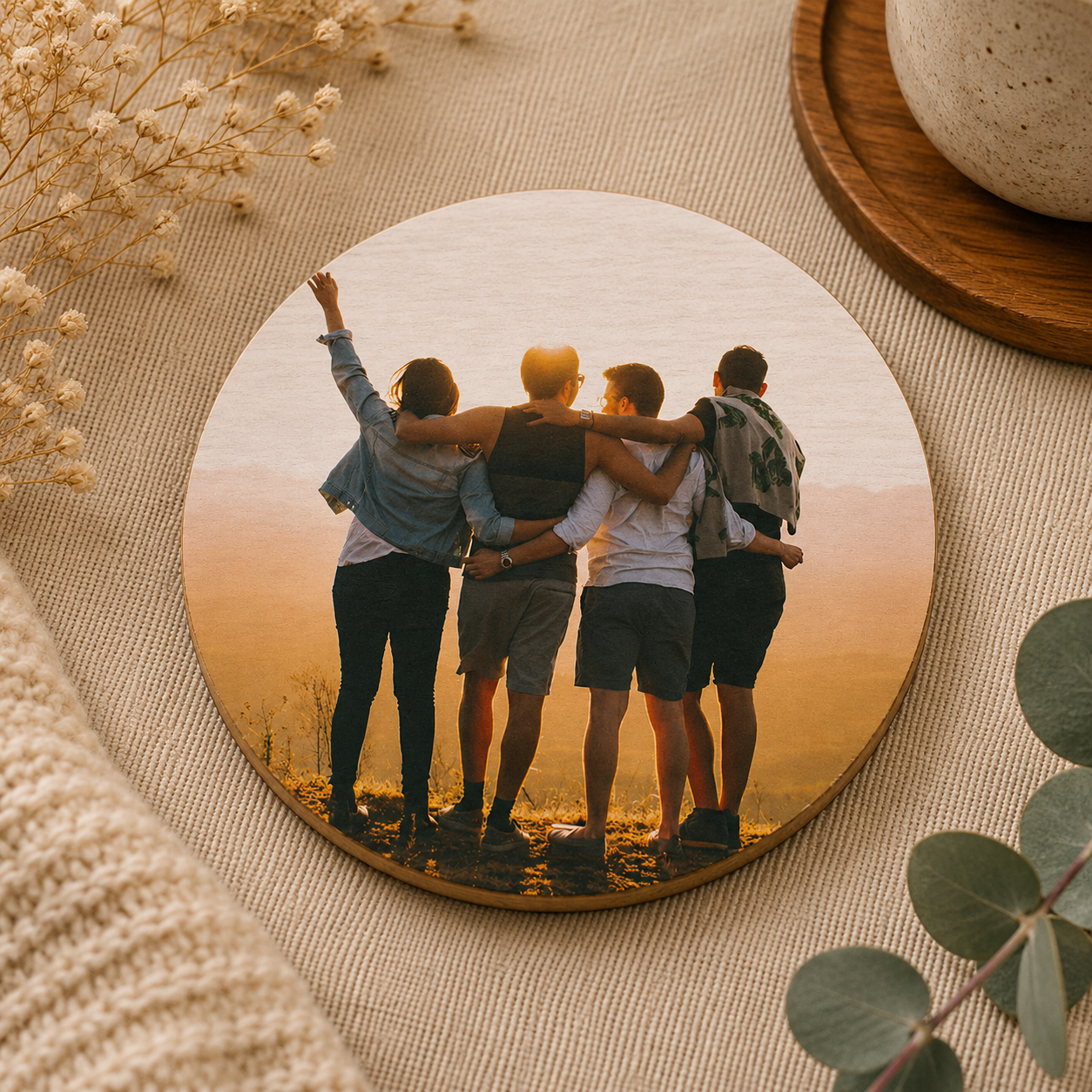 A round wooden coaster personalised with a photo of a group of friends on a neutral background with plant pots.
