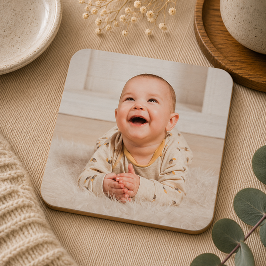 Square wooden coaster personalised with a photo of a baby clapping on a beige surface with decorative elements.