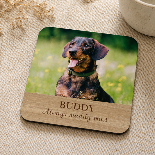 Square personalised wooden coaster with a dog photo and 'Buddy Always muddy paws' text on a textured surface.