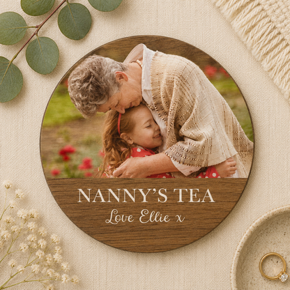 Circular wooden coaster personalised with a family photo, surrounded by greenery and flowers, with 'Nanny's Tea' text.