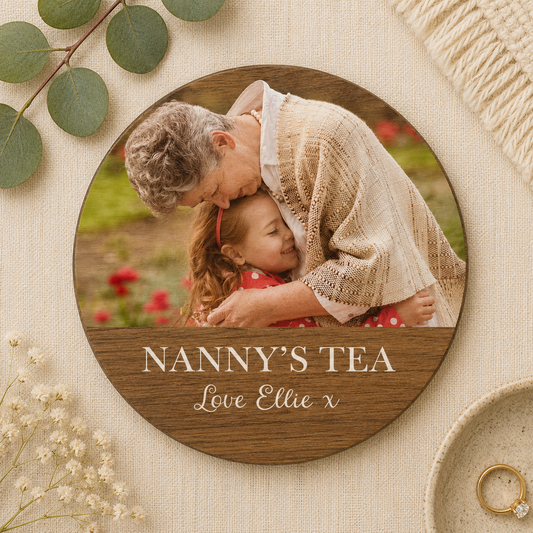 Circular wooden coaster personalised with a family photo, surrounded by greenery and flowers, with 'Nanny's Tea' text.