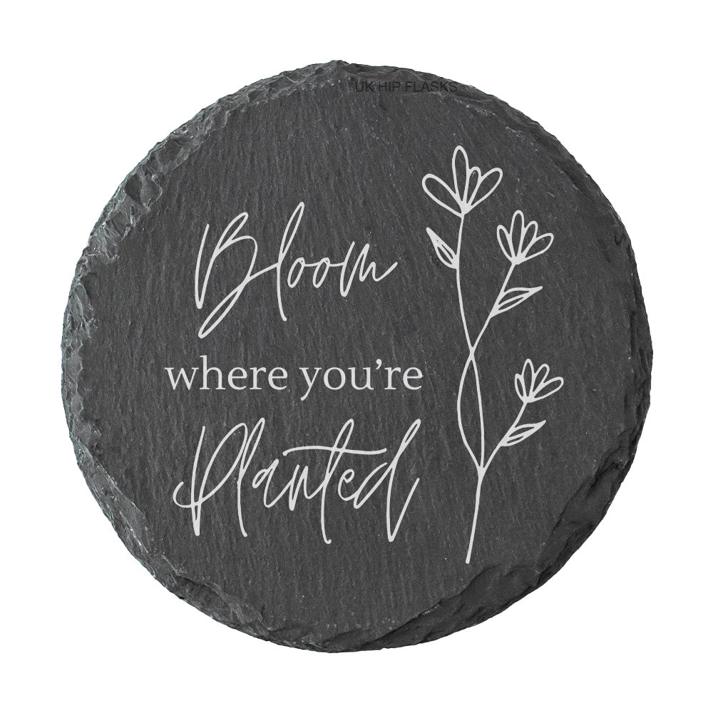 Round slate coaster with "Bloom where you're planted" quote in white text.