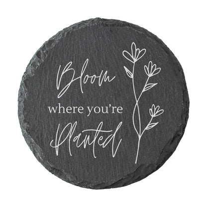 Round slate coaster with "Bloom where you're planted" quote in white text.
