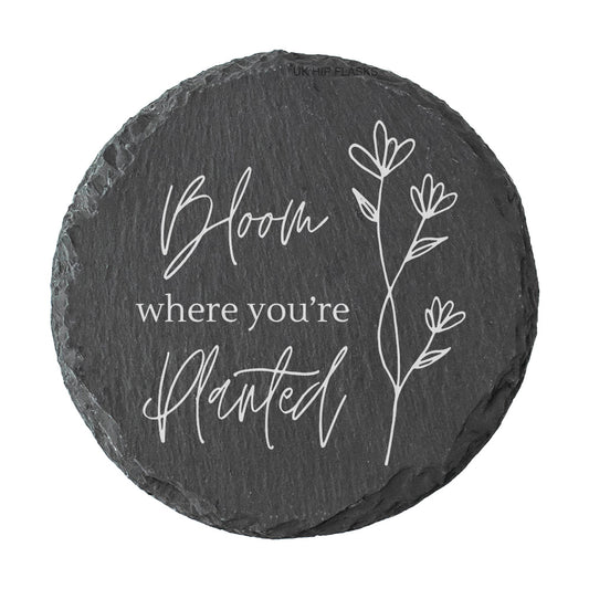 Round slate coaster with "Bloom where you're planted" quote in white text.
